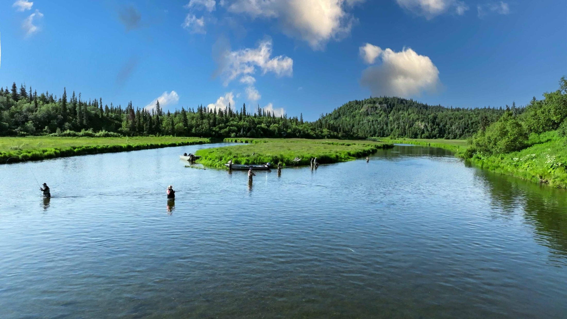 Anglers wading a wide clear river under blue skies near Legend Lodge, Alaska
